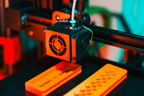 3D printer nozzle printing small orange plastic parts
